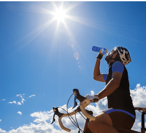Cyclist resting and drinking isotonic drink. Backlight, sunny summer day.