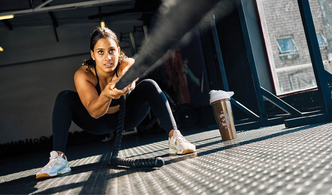 Female athlete pulling a weighted sled in a gym. Front view of a woman performing strength training exercise on a black gym floor. Hyrox Training Concept.