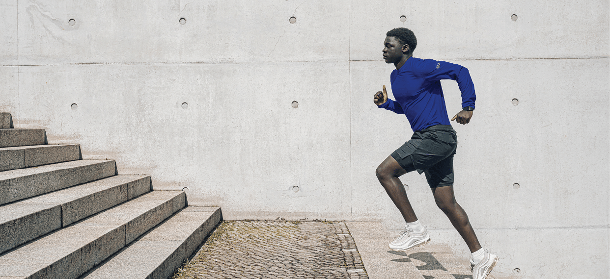 young sportsman running up steps in front of concrete wall outdoors in berlin at sunny day