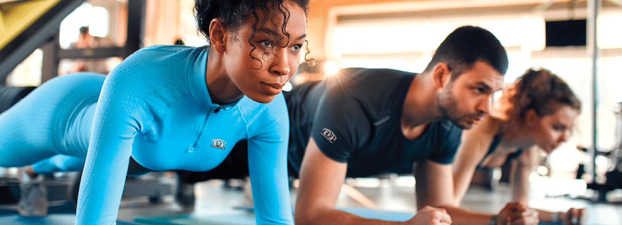 Slim women african american and caucasian ethnicity and muscular man in sportswear doing plank exercise on rubber mat in gym club. The concept of sports and recreation.